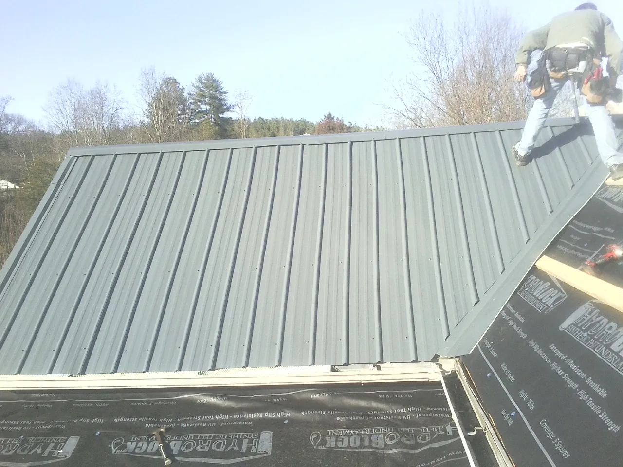 Crew installing dark green standing seam panels over synthetic underlayment in Hillsboro